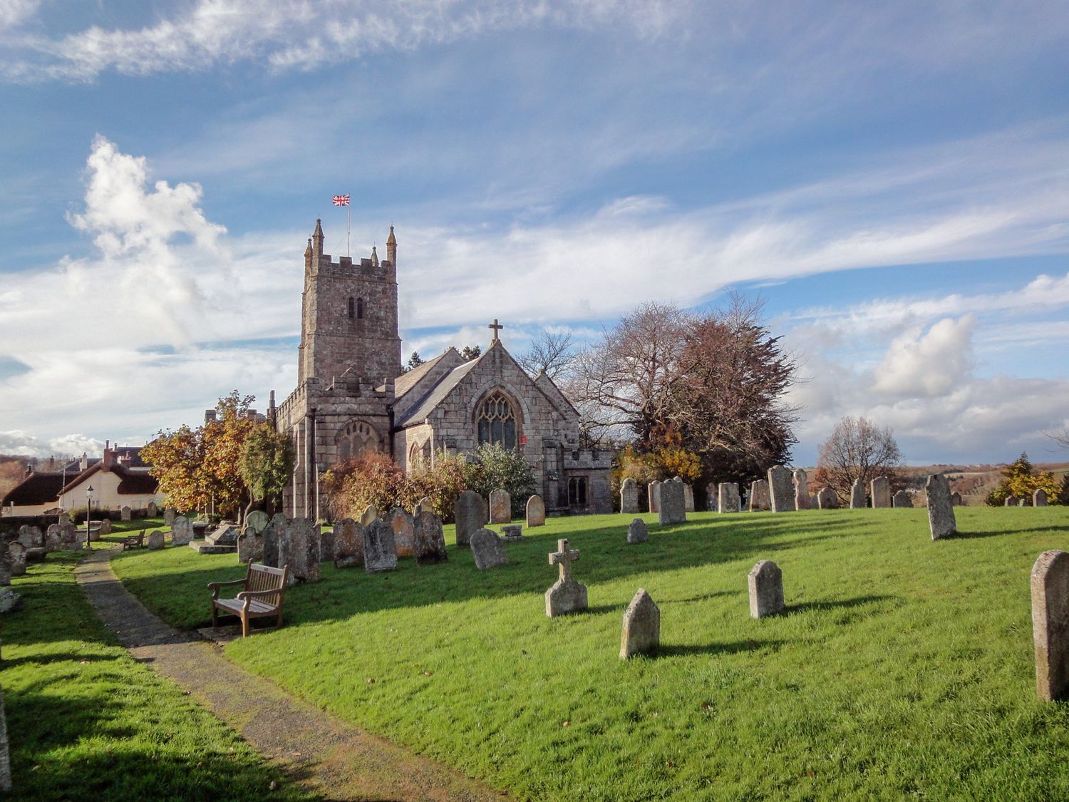 A church with a tower and surrounding gravestones in a grassy churchyard at Rookwood in Drewsteignton