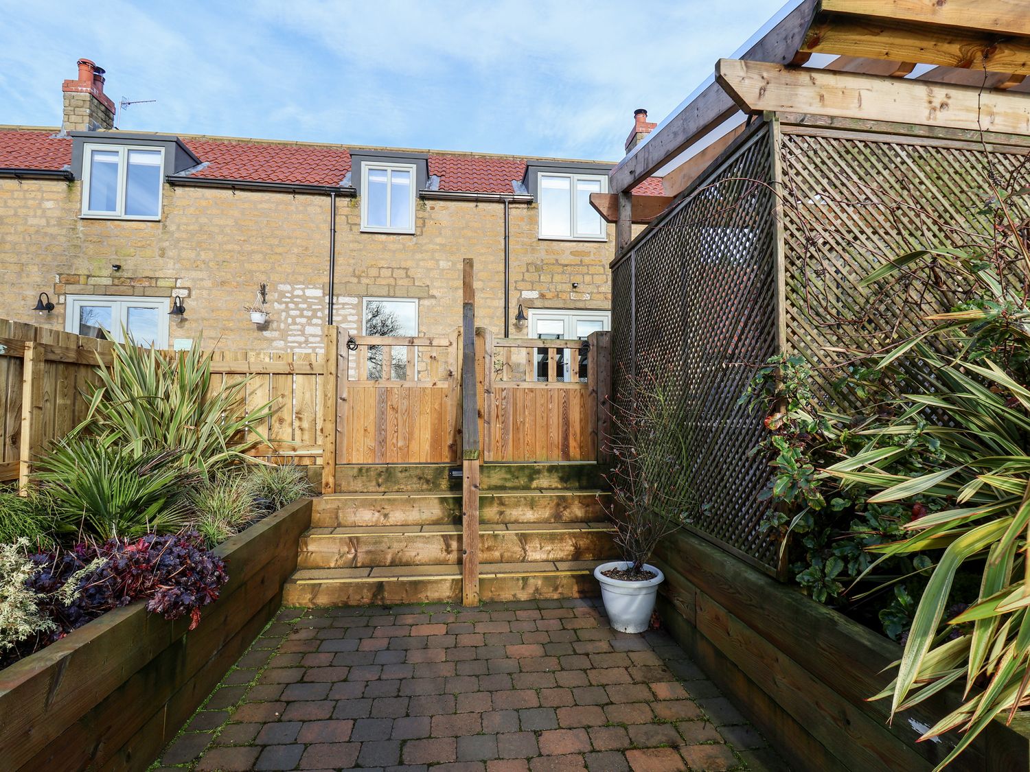 A backyard garden with wooden fencing plants and stone steps leading to a two story stone house at Tawny Cottage in Irton Moor near Scarborough