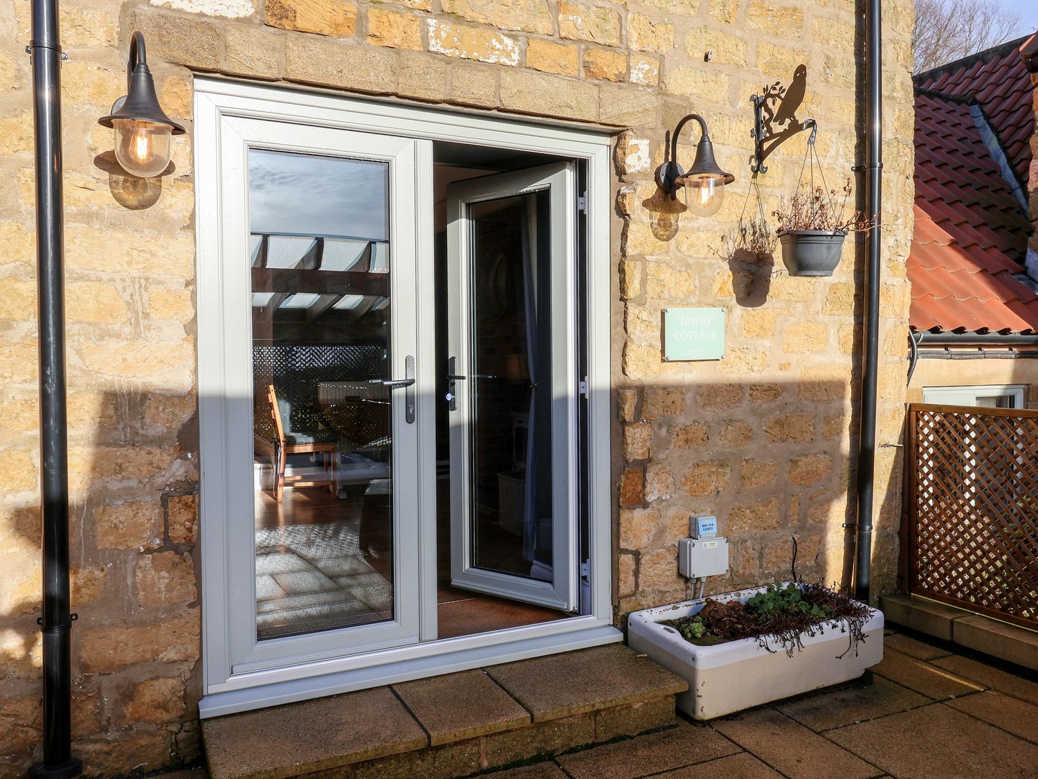 Exterior stone wall with glass double doors a hanging plant two wall lamps and a planter at Tawny Cottage Irton Moor near Scarborough