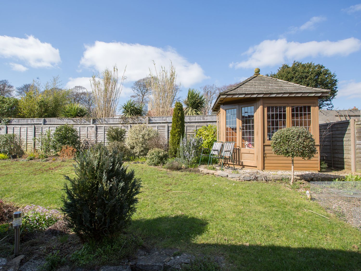 A garden with a wooden summerhouse surrounded by plants and grass at Connaught Gardens Weymouth