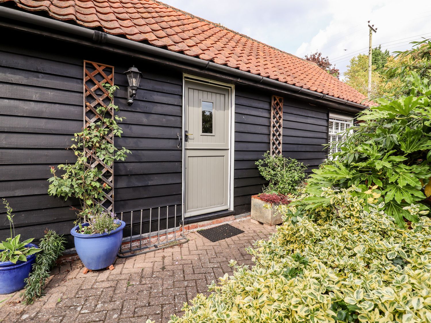 A black wooden exterior wall with a gray door and plants in blue pots at Courtyard Cottage Poplar Farm Barn Sweffling near Saxmundham