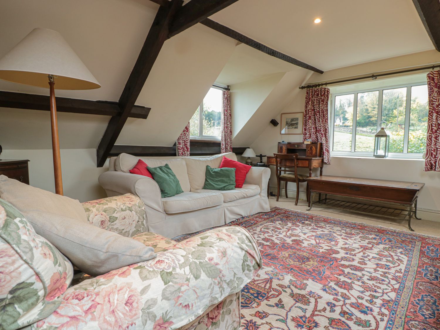 A living room with sofas pillows a lamp wooden desk and windows at Little End Amberley near Stroud