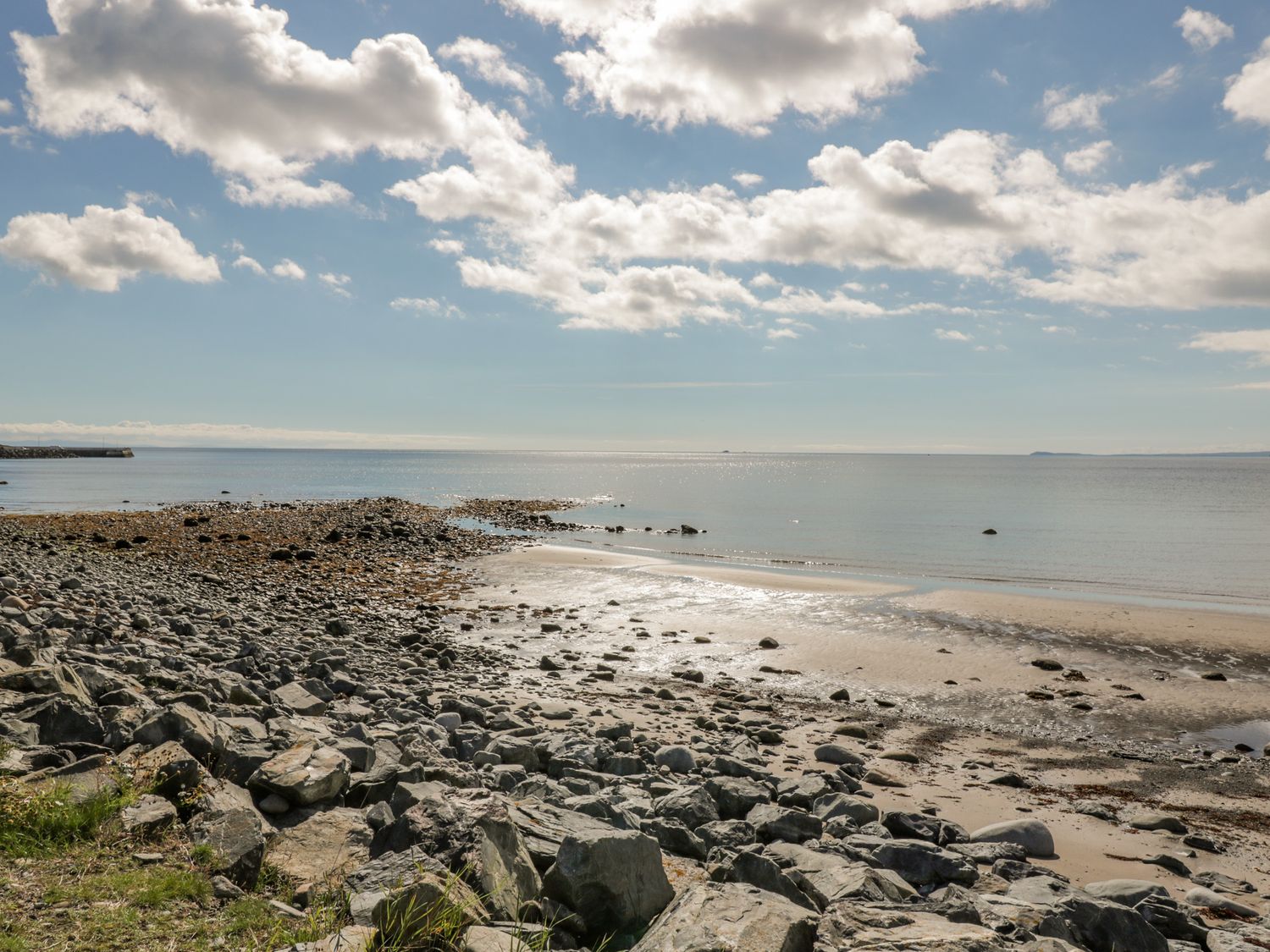 A rocky beach with some sand and calm sea under a partly cloudy sky at Greystones in Port William