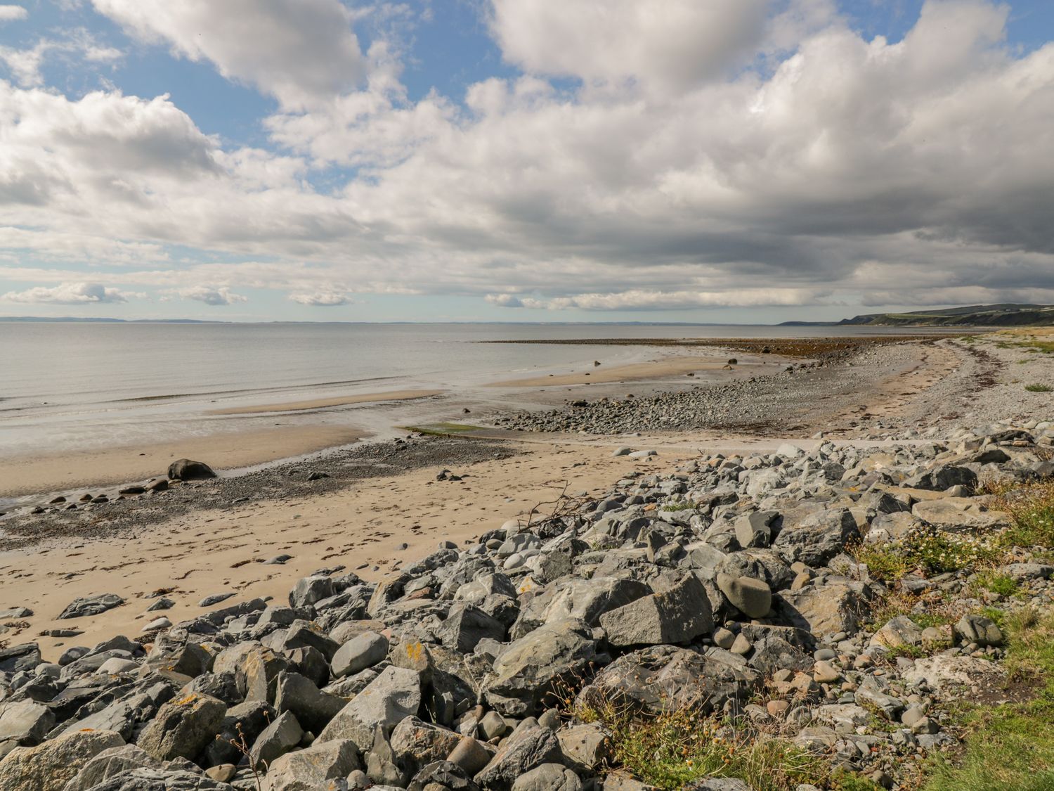 A rocky and sandy beach with calm sea under a partly cloudy sky at Greystones in Port William