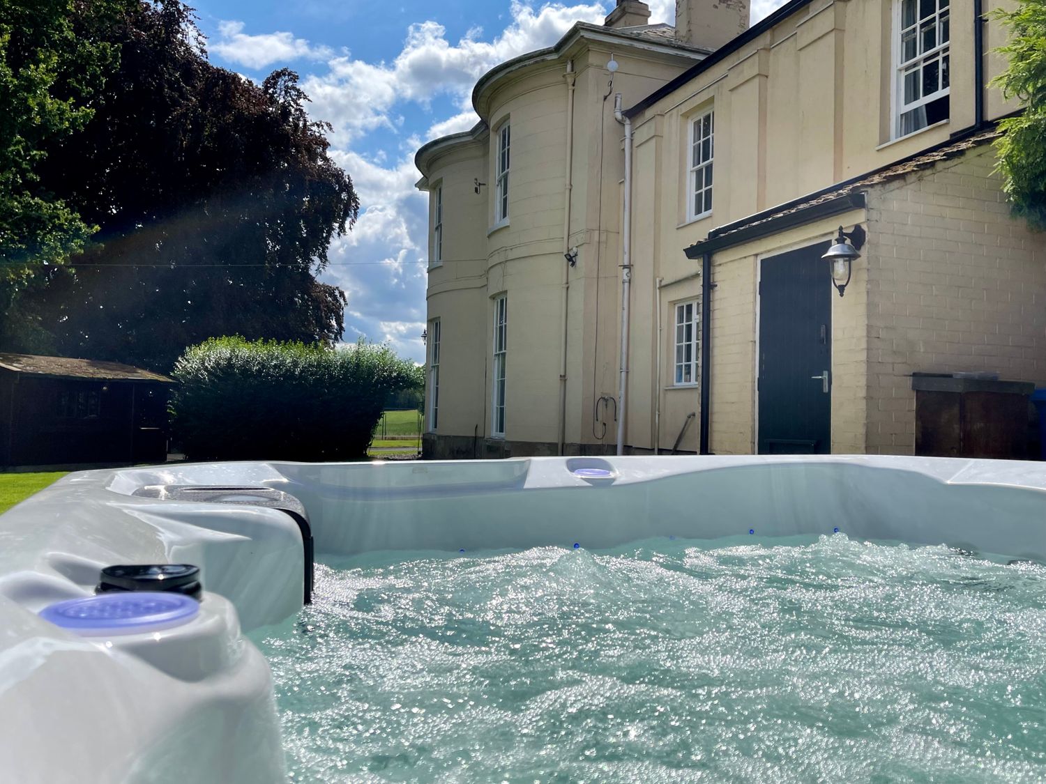 A bubbling hot tub outside a cream colored house with a green door and garden at Moortown House in Caistor
