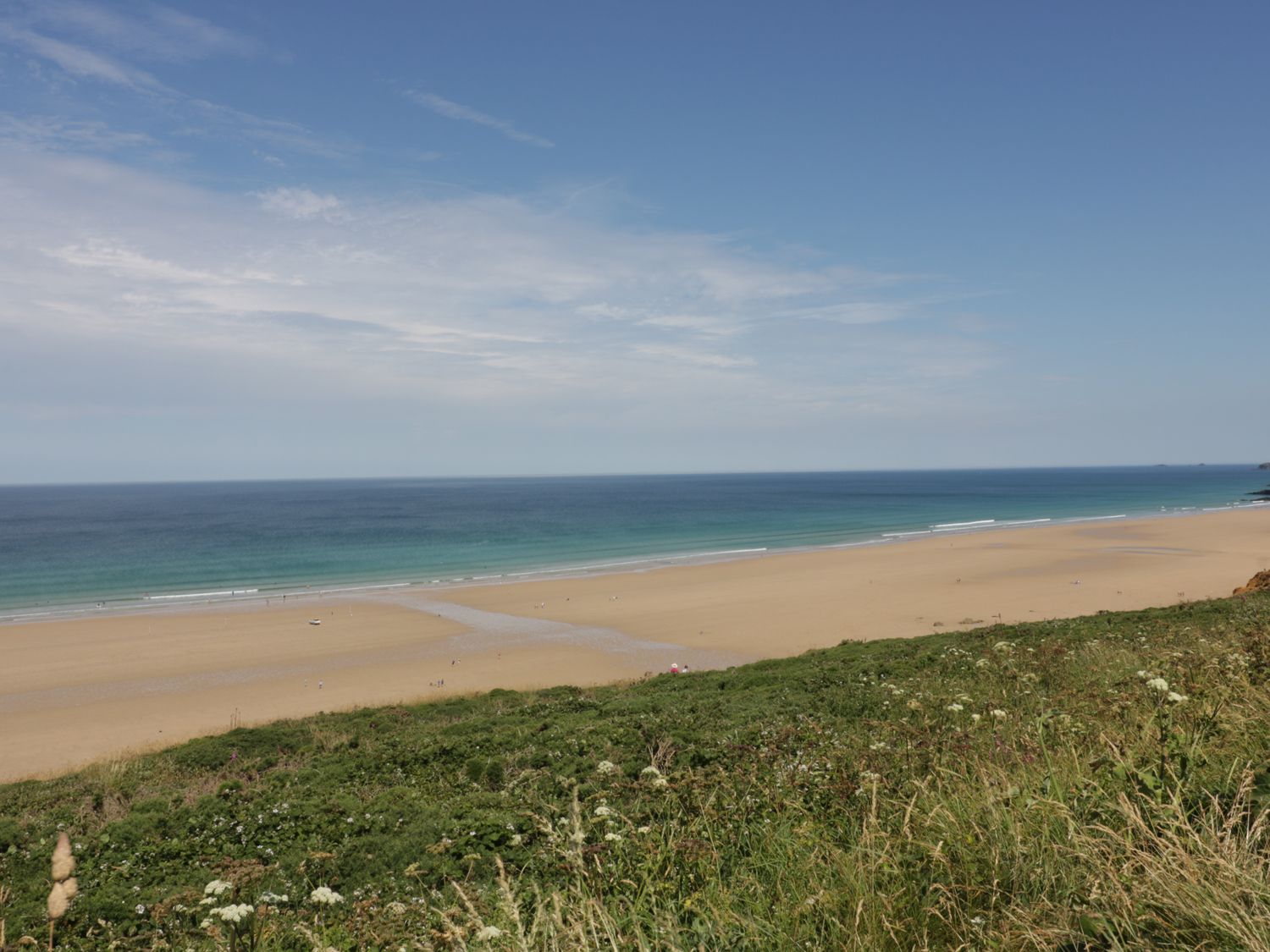 A sandy beach with people near the ocean and grassy vegetation in the foreground at The Coach House in Goonhavern