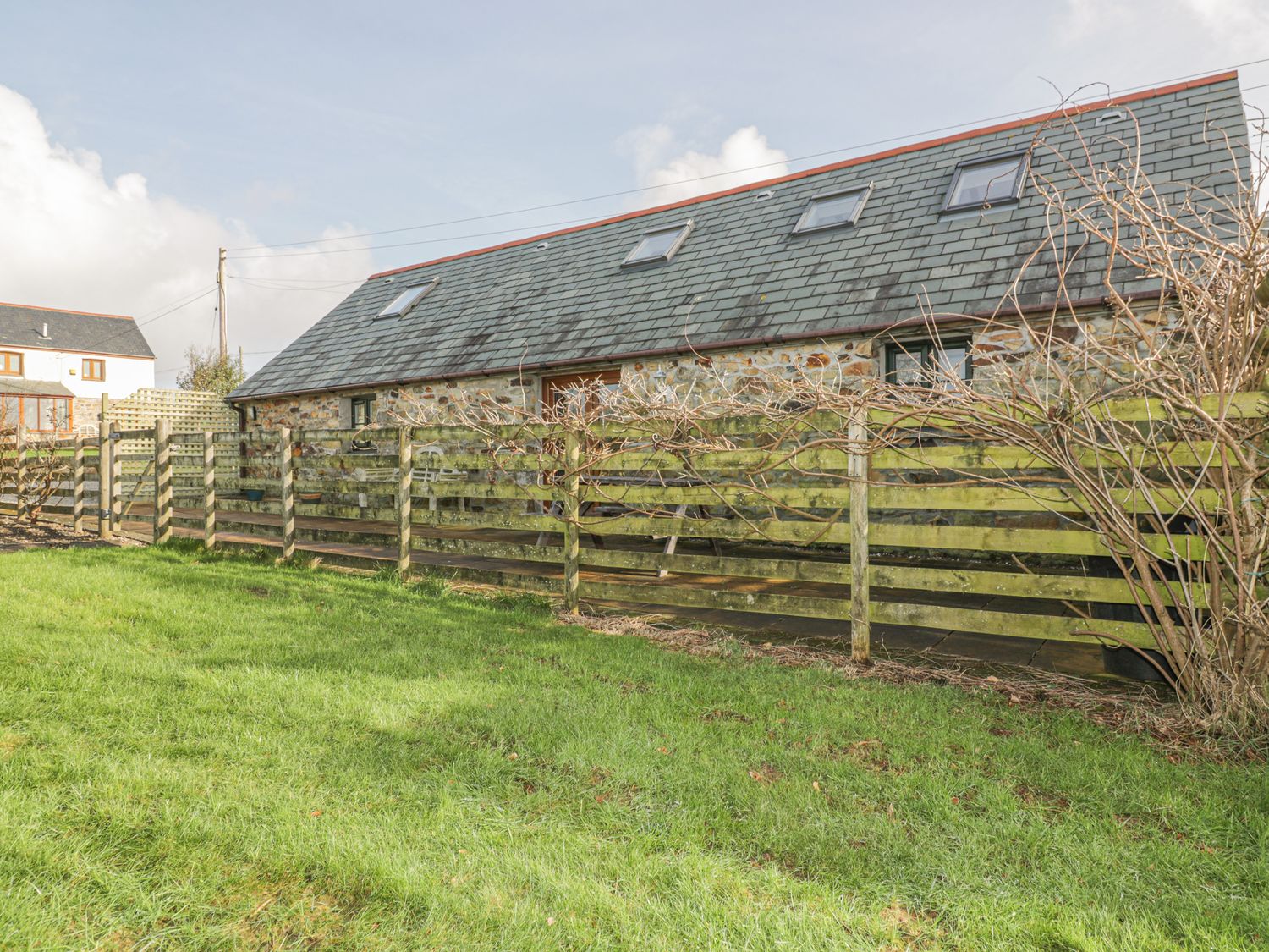 A stone house with a slate roof and skylights behind a wooden fence and a garden at The Coach House in Goonhavern