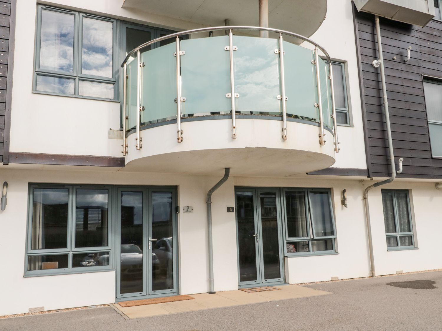 The exterior of a modern building with two doors numbered 6 and 7 and a balcony with glass panels above Apartment 7 in West Bay