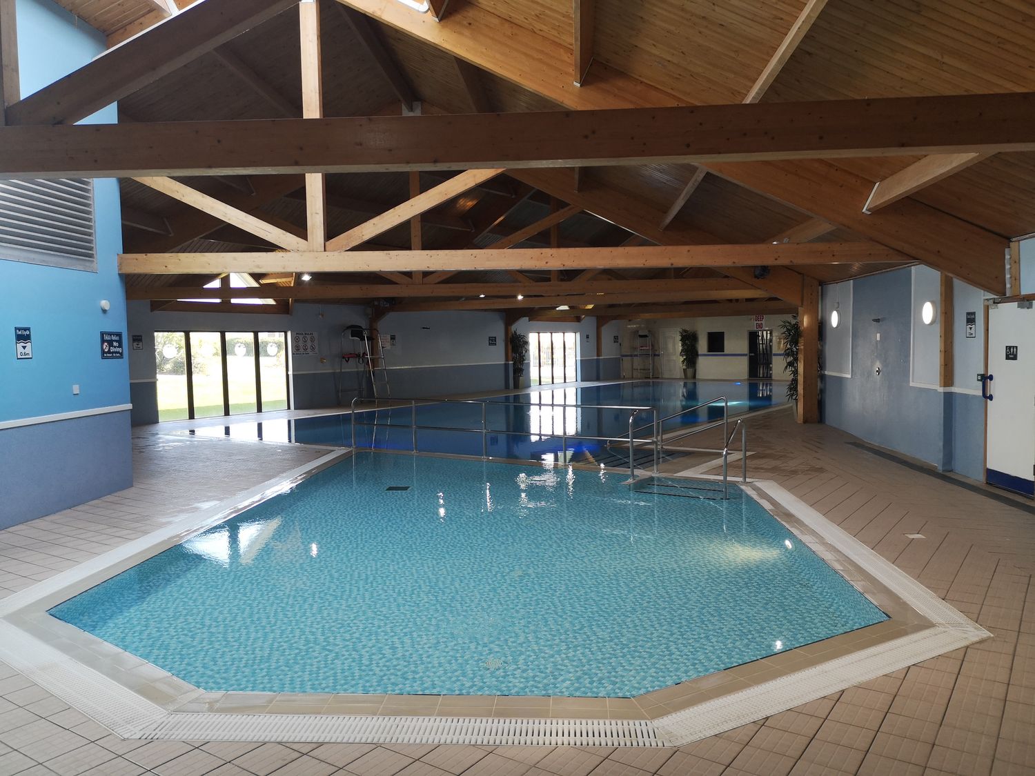 An indoor swimming pool area with wooden beams on the ceiling and two connected pools at Victoria Cottage in Amble