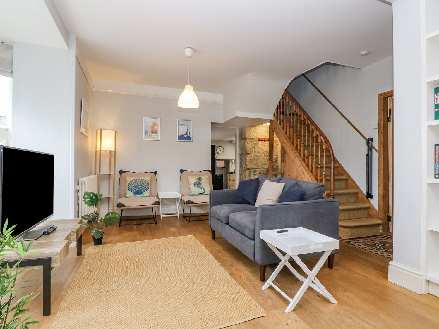 A living room with a gray sofa two chairs a television on a stand and wooden stairs at Mackerel Sky in Penzance