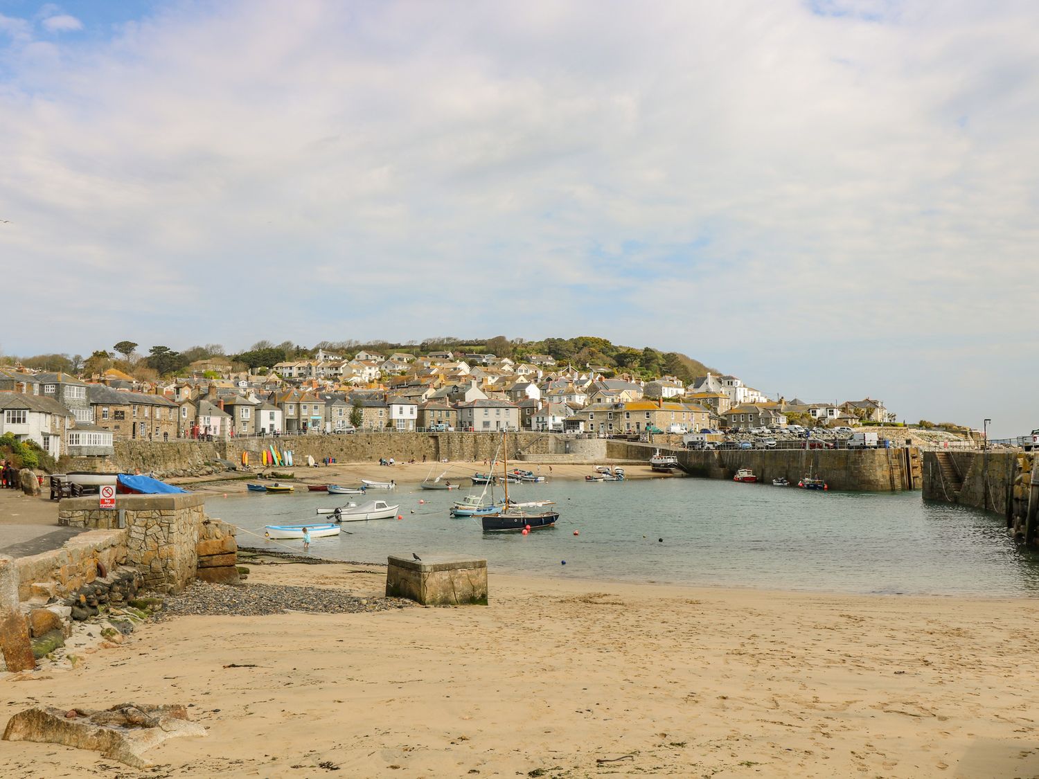 A small harbor with boats on water and sandy beach with stone walls and houses in the background at Mackerel Sky in Penzance