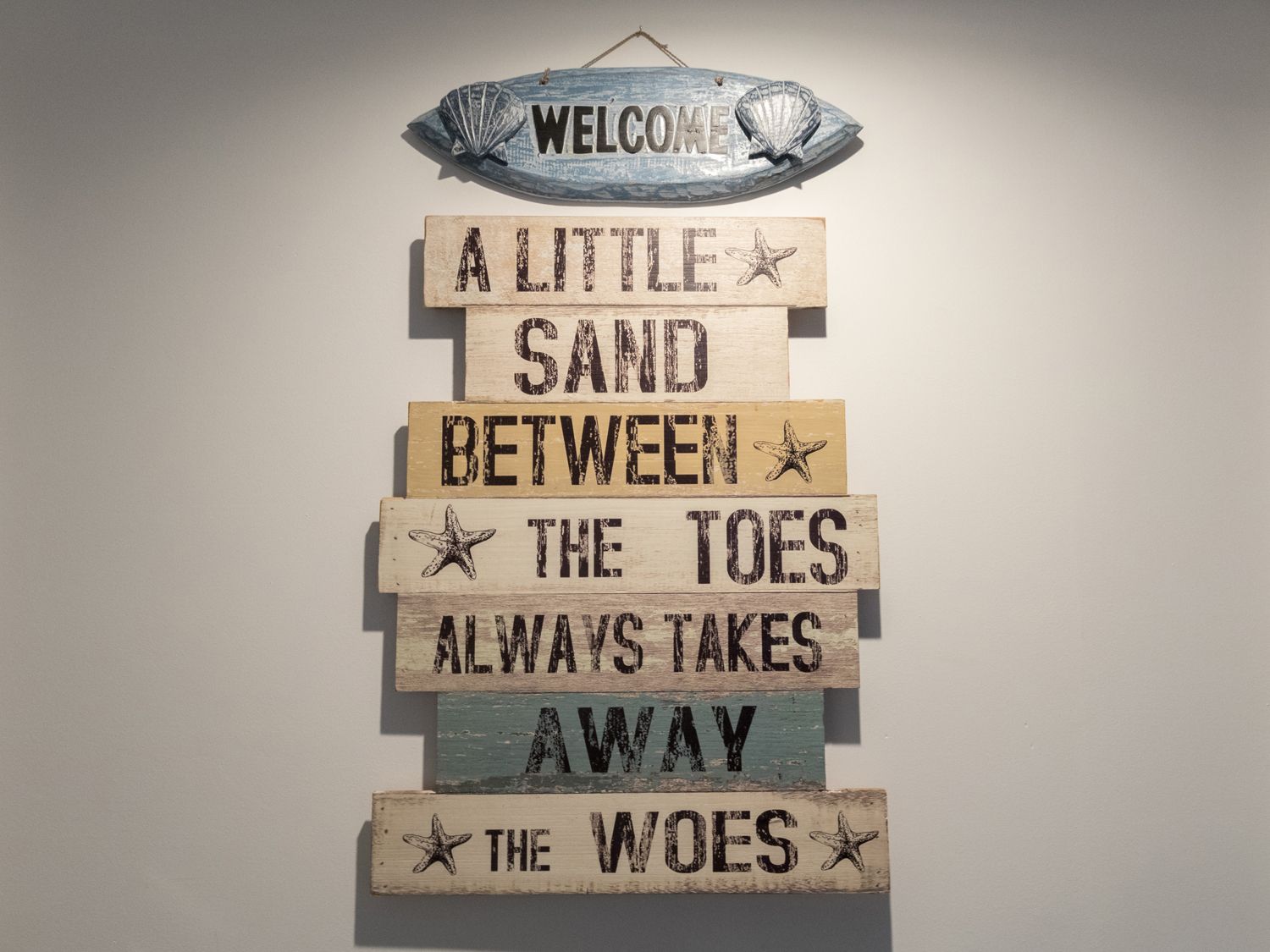 A wall decoration with a welcome sign and a wooden sign with a beach quote at 6 The Beaches in Weymouth