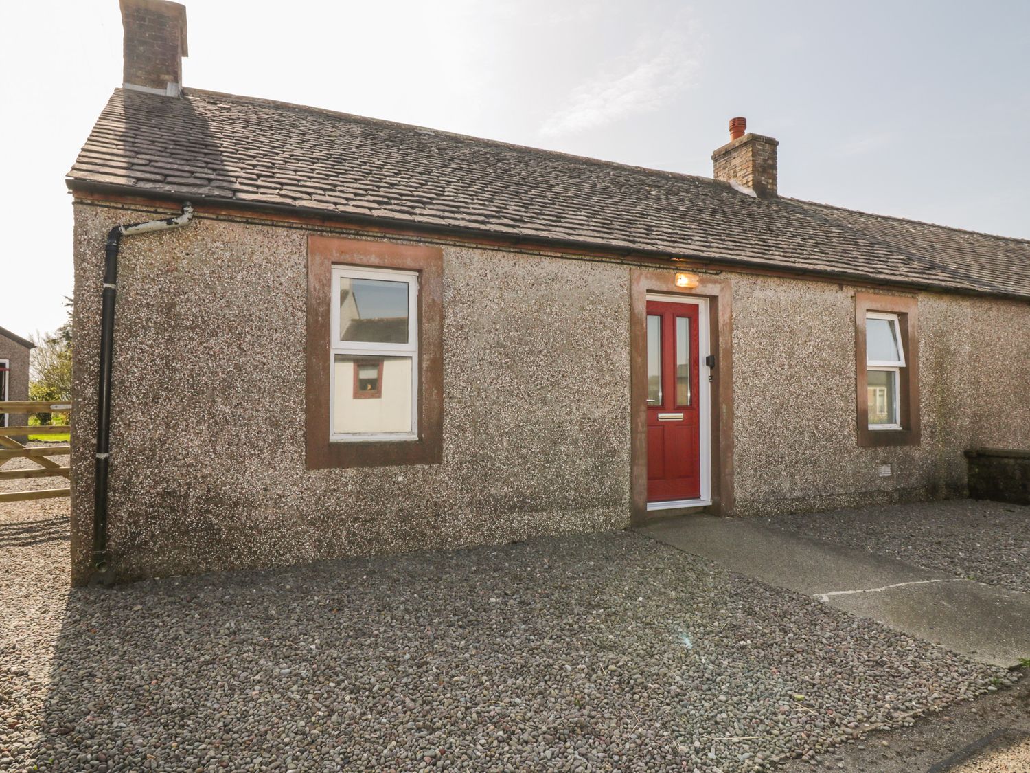 A single-story house with two windows and a red door on a gravel front at 7 Cummertrees in Cummertrees near Annan