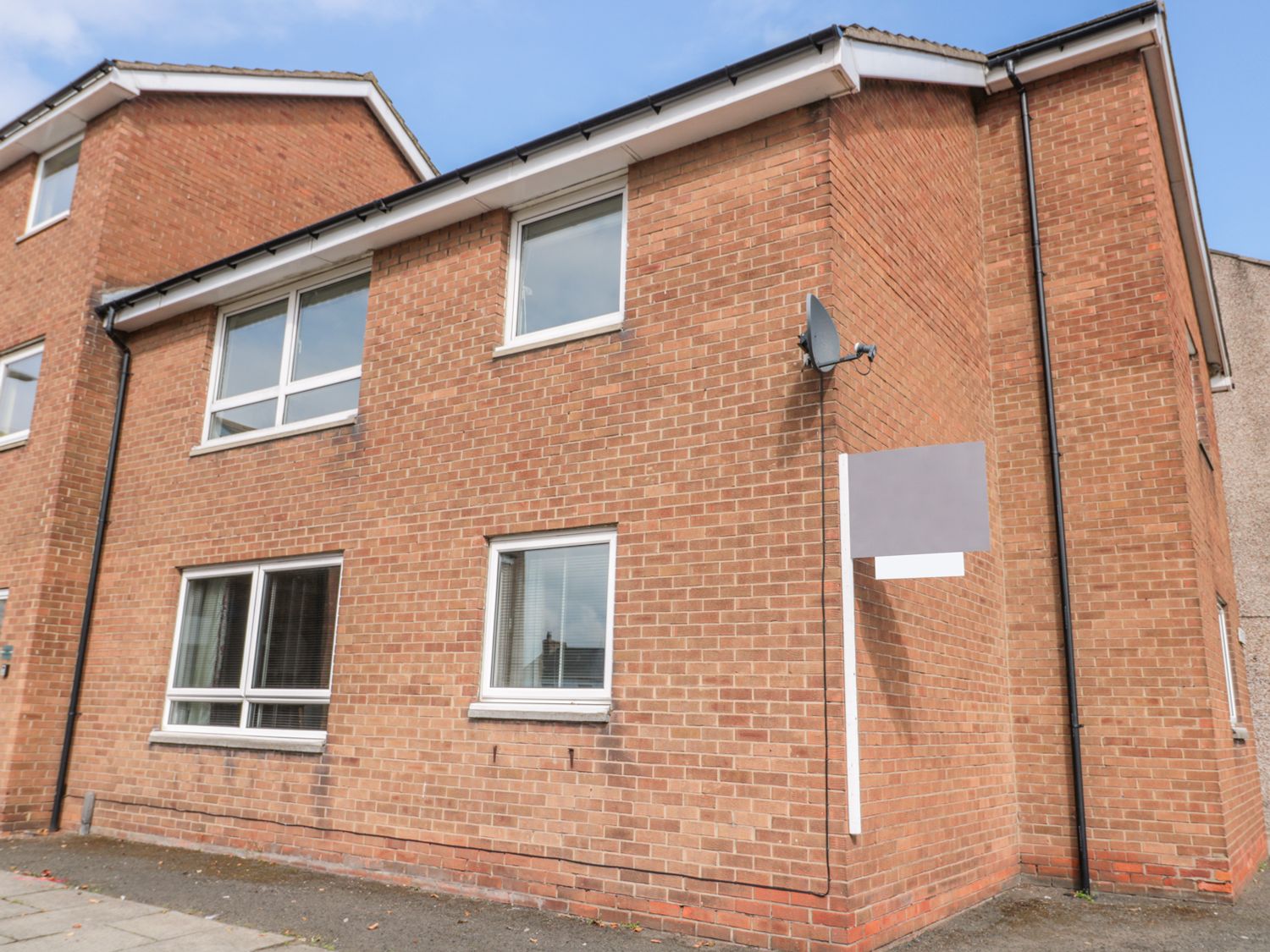 A brick residential building with multiple windows and a satellite dish on the wall at The Wynd Apartment in Amble