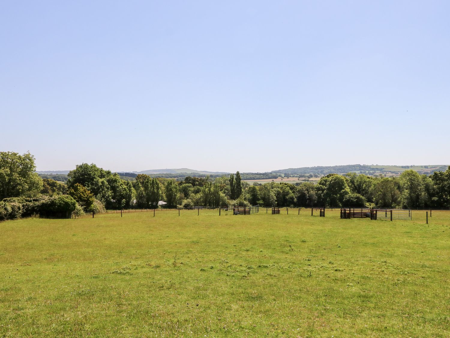 A grassy field with fenced animal enclosures and trees in the distance at 1 The Stables in Ryde