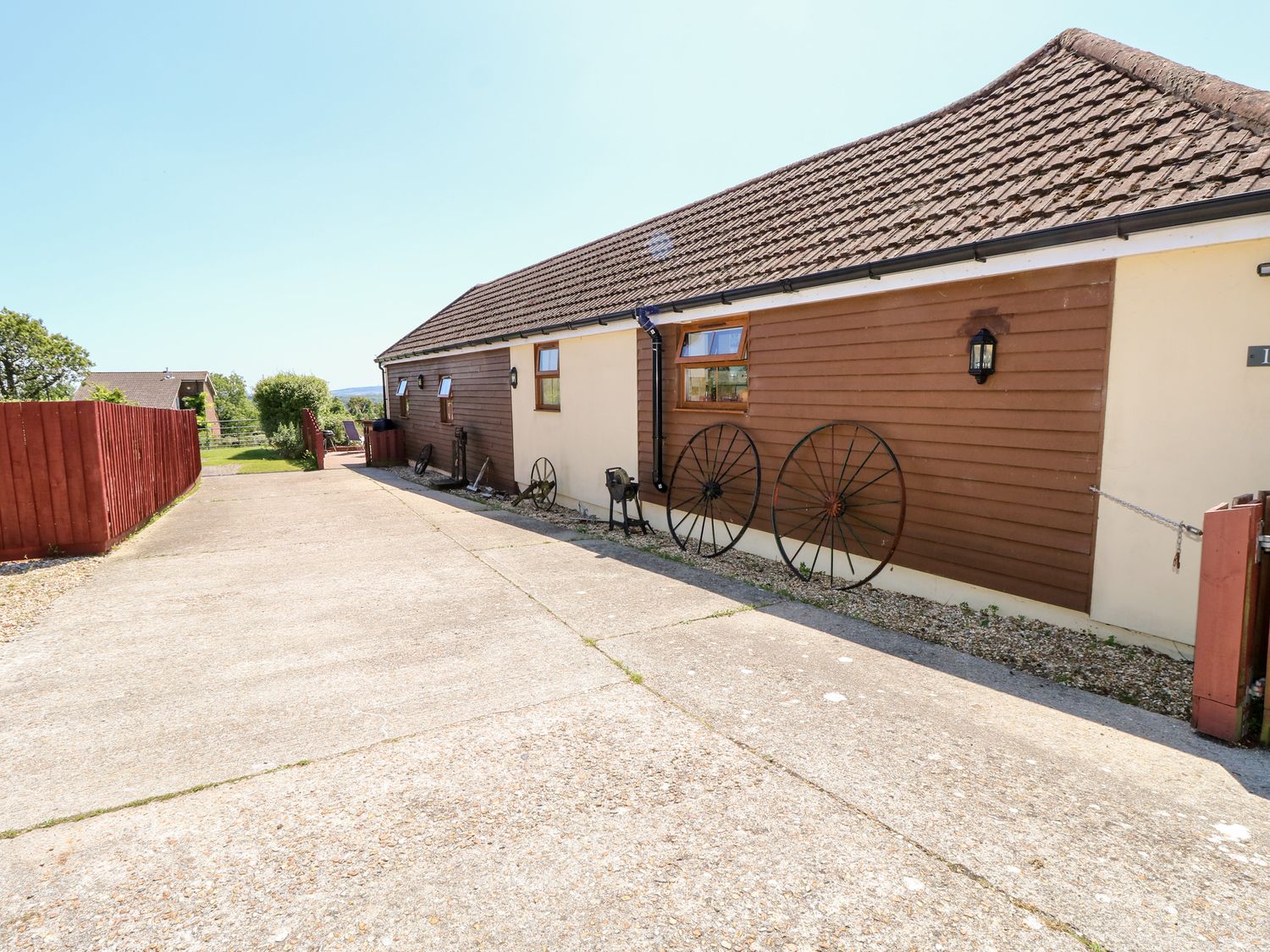 The exterior of a building with a tiled roof and brown cladding with old wagon wheels along the wall at 1 The Stables in Ryde