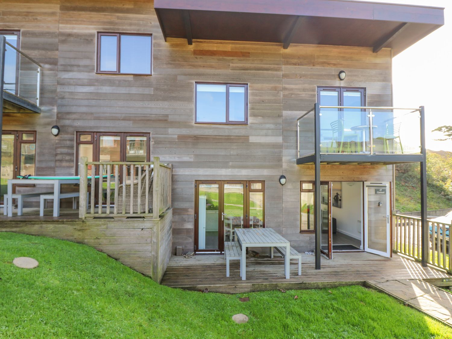 The exterior of a modern wooden building with a small patio area and balcony at Sea Breeze 17 Gannel in Porthtowan
