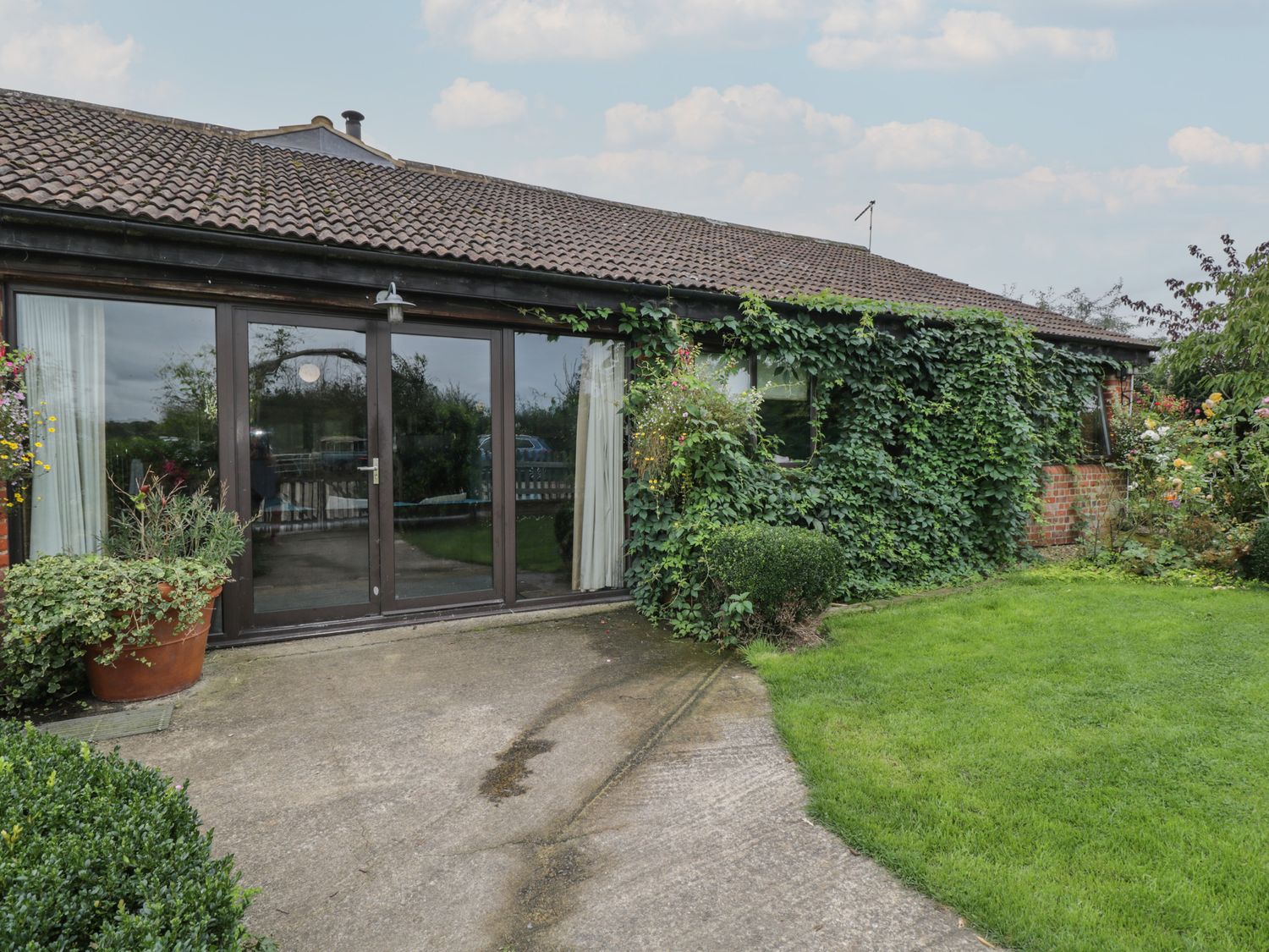 The exterior of a single-story building with large glass doors surrounded by greenery and plants at The Barn in Draycot Cerne near Malmesbury