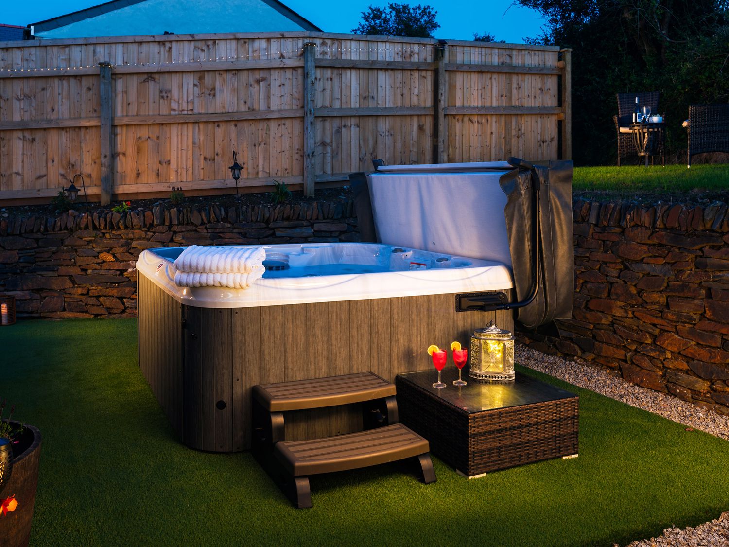 An outdoor hot tub on artificial grass with steps towels drinks and a lantern at Be Our Guest Cottage in Chacewater near Truro