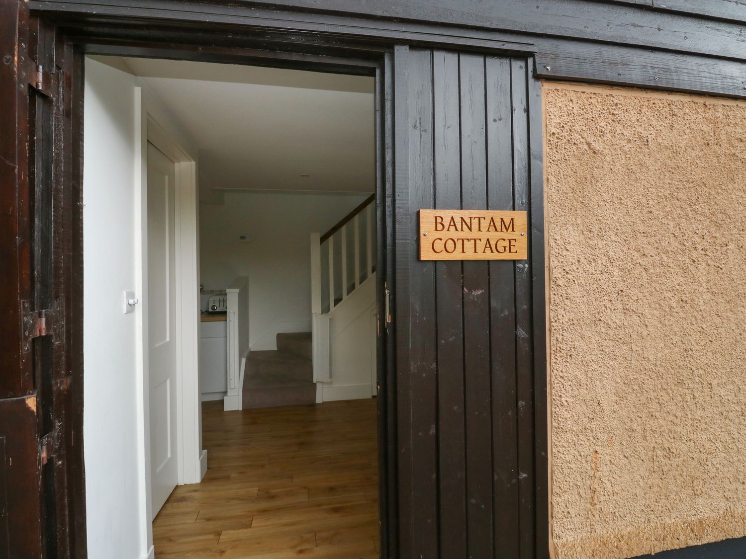 An open door with a wooden floor visible inside and stairs in the background at Bantam Cottage Little Woodford near Ottery St Mary