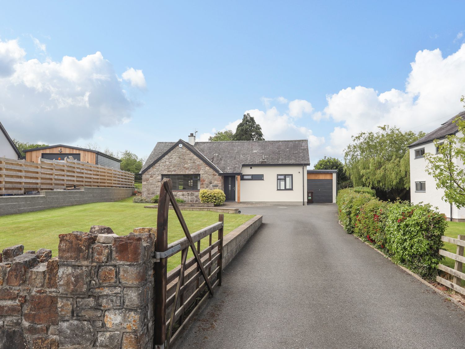 A bungalow with a stone wall facade and attached garage with a driveway and lawn at Bronallt in Y Felinheli