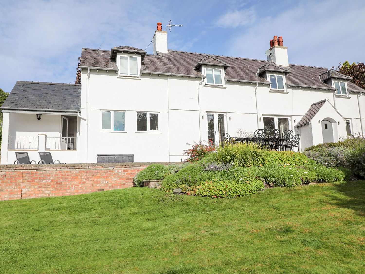 A white two story house with a grey roof and garden furniture on a patio at Cae Gallt in Menai Bridge