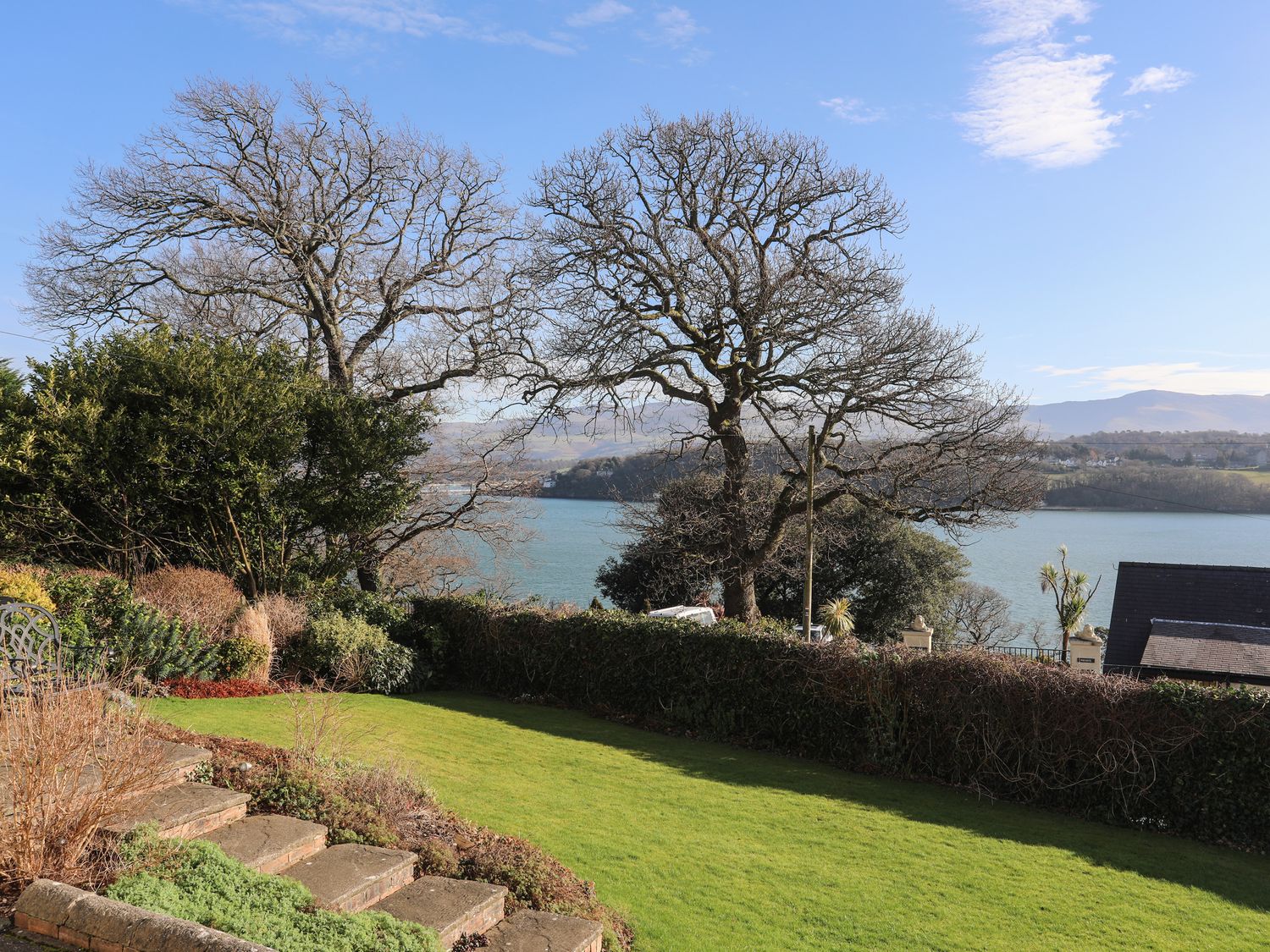 A garden with trimmed grass and leafless trees overlooking a body of water at Cae Gallt in Menai Bridge