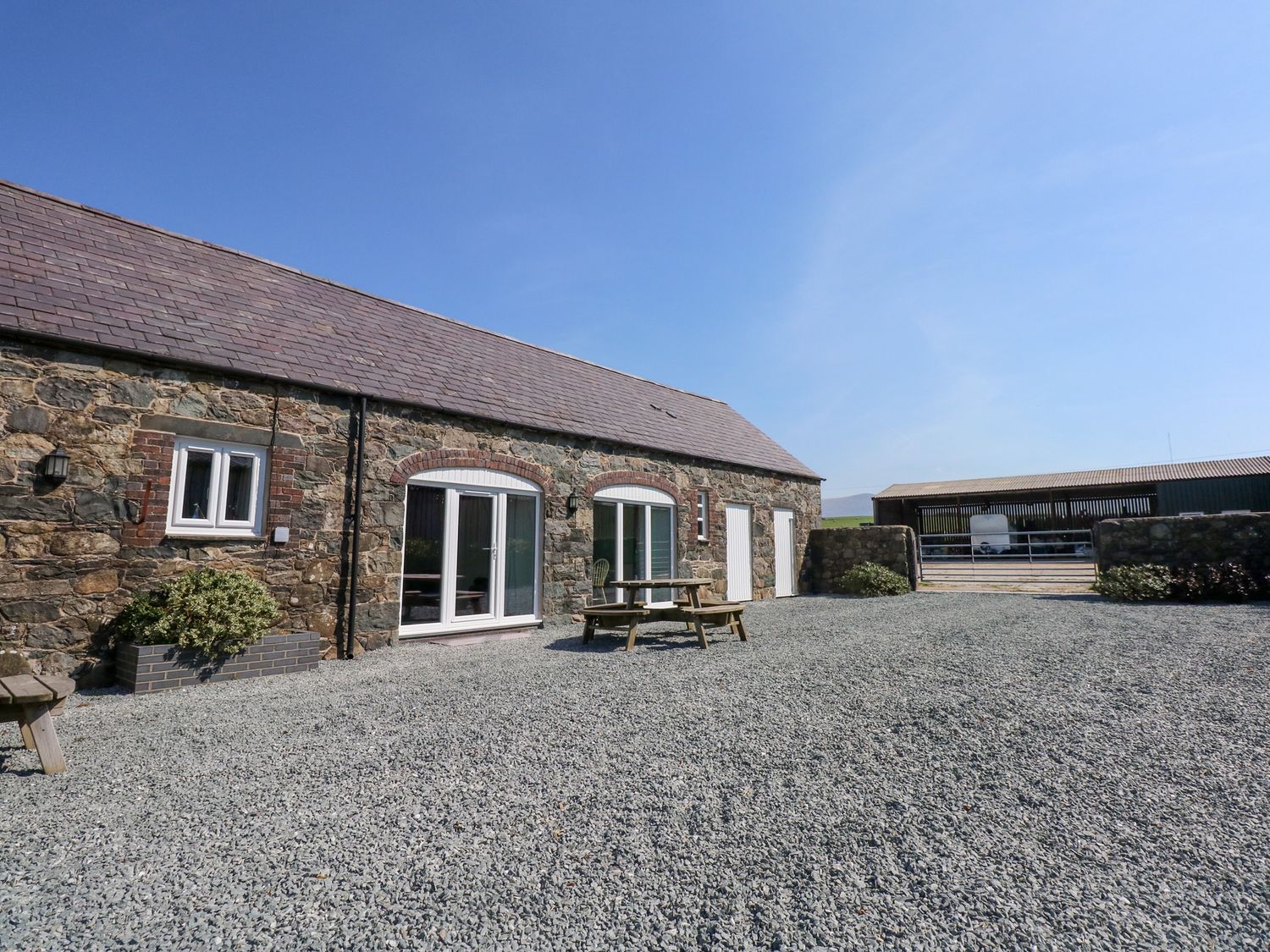 A stone building with white doors and windows a wooden picnic table and gravel ground at Hafod in Pontllyfni