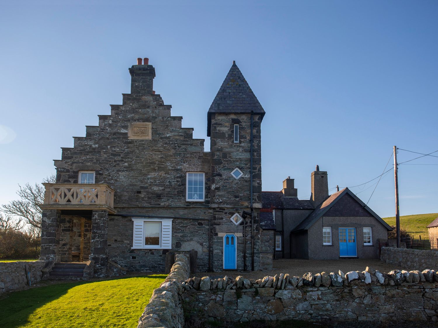 Stone house with blue doors and windows and a small balcony surrounded by a stone wall at Plas in Rhoscolyn