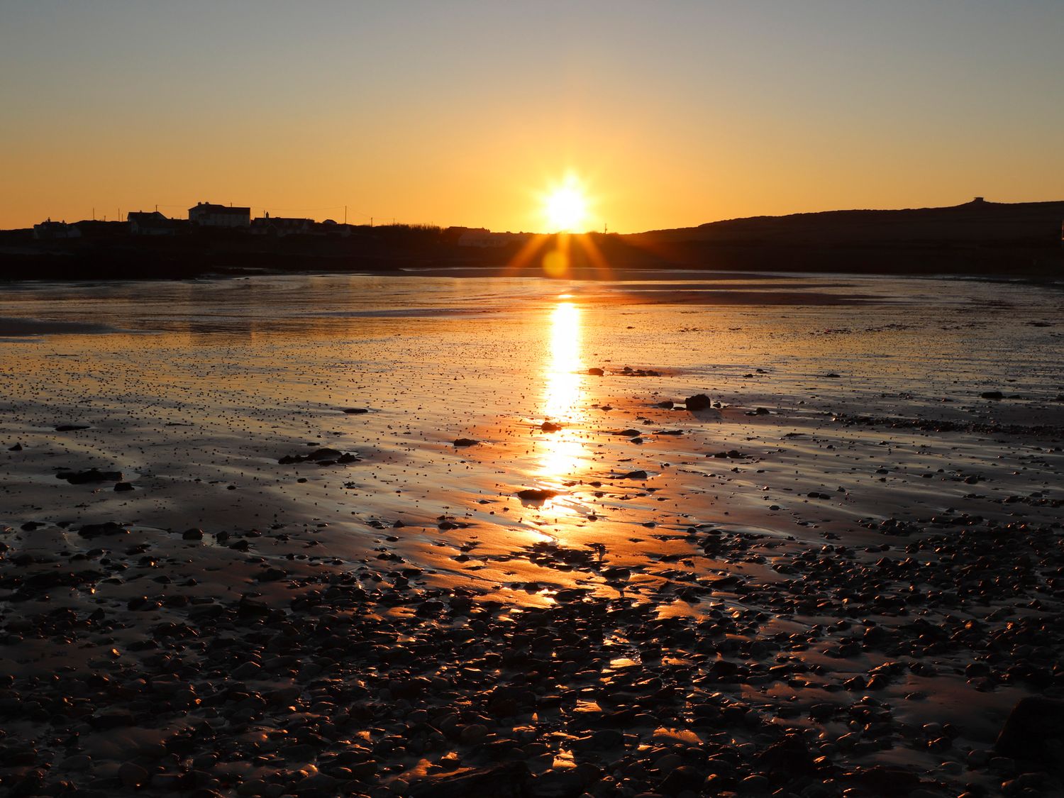 A sunset over a rocky beach with water reflecting the sun at Plas in Rhoscolyn