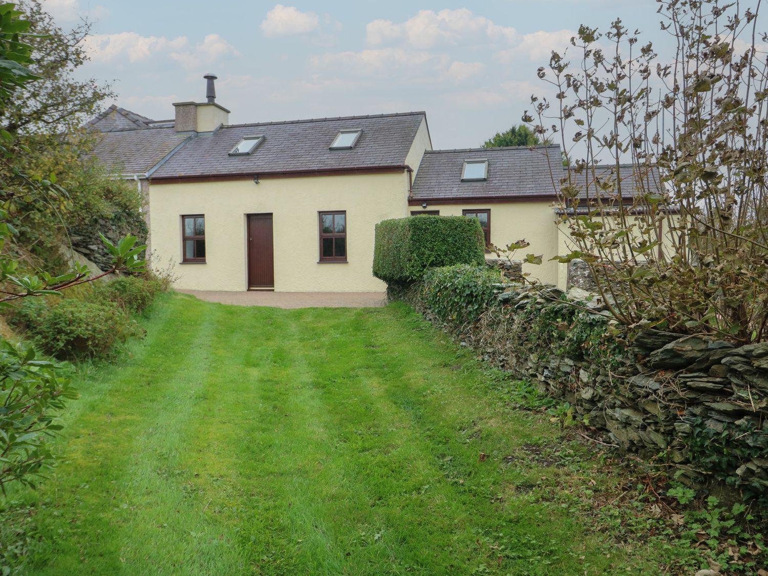 A cottage with a door and windows surrounded by grass and a stone wall at Tyn y Mynydd Bull Bay