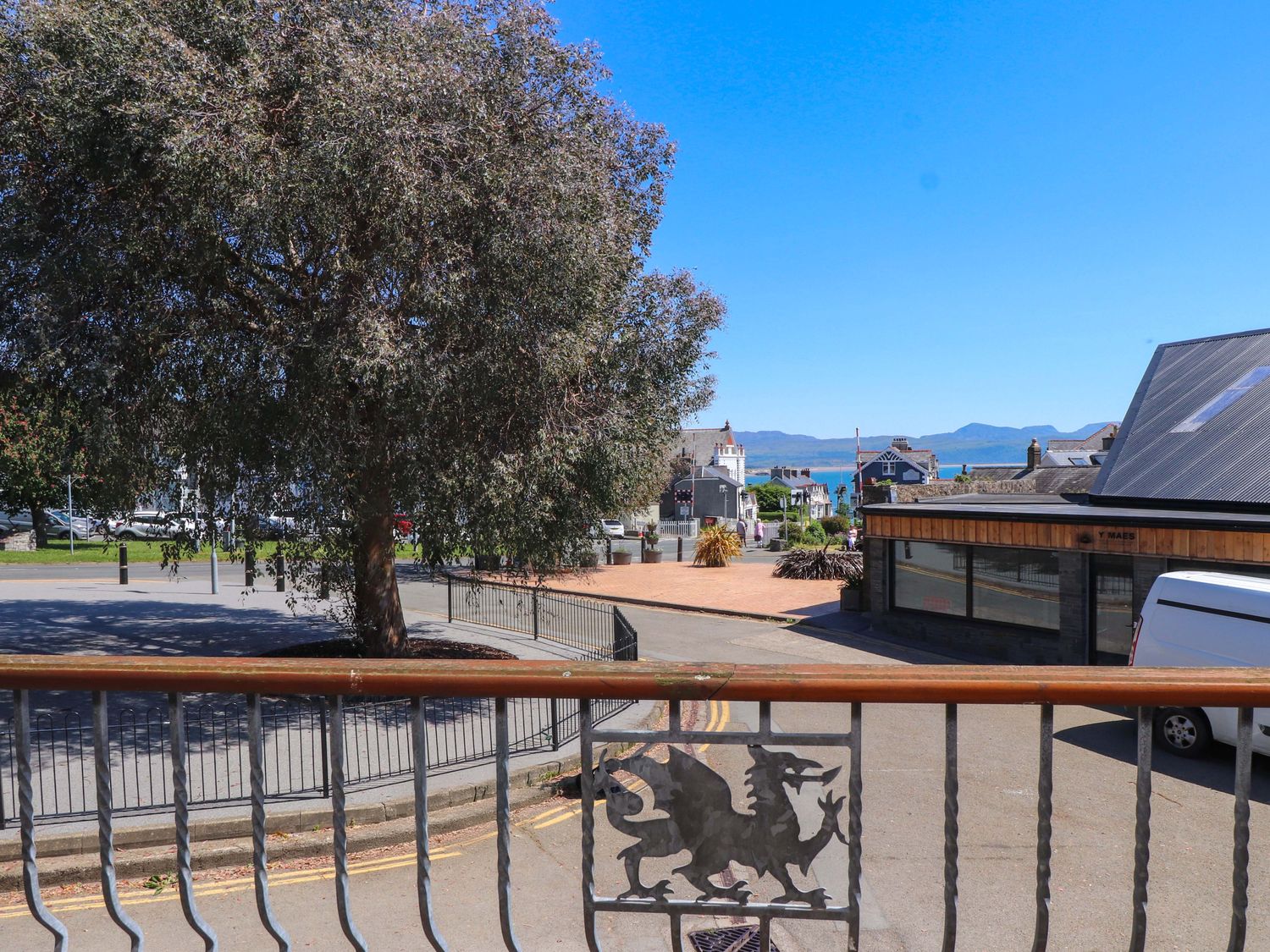 A street view with a tree on the left a building on the right and mountains in the background at Y Stabl in Criccieth