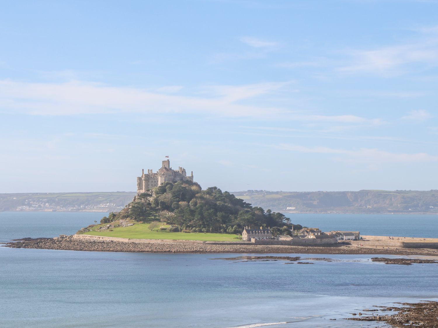 A castle on a small island surrounded by water with buildings at the base and hills in the background at Tinners Rest in Pendeen