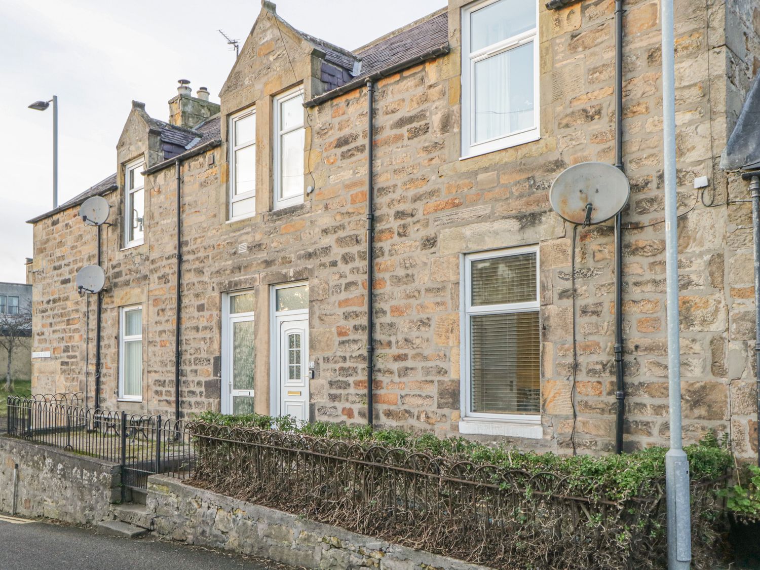 A stone terraced house with white doors and windows and metal railings in front at The Neuk in Elgin