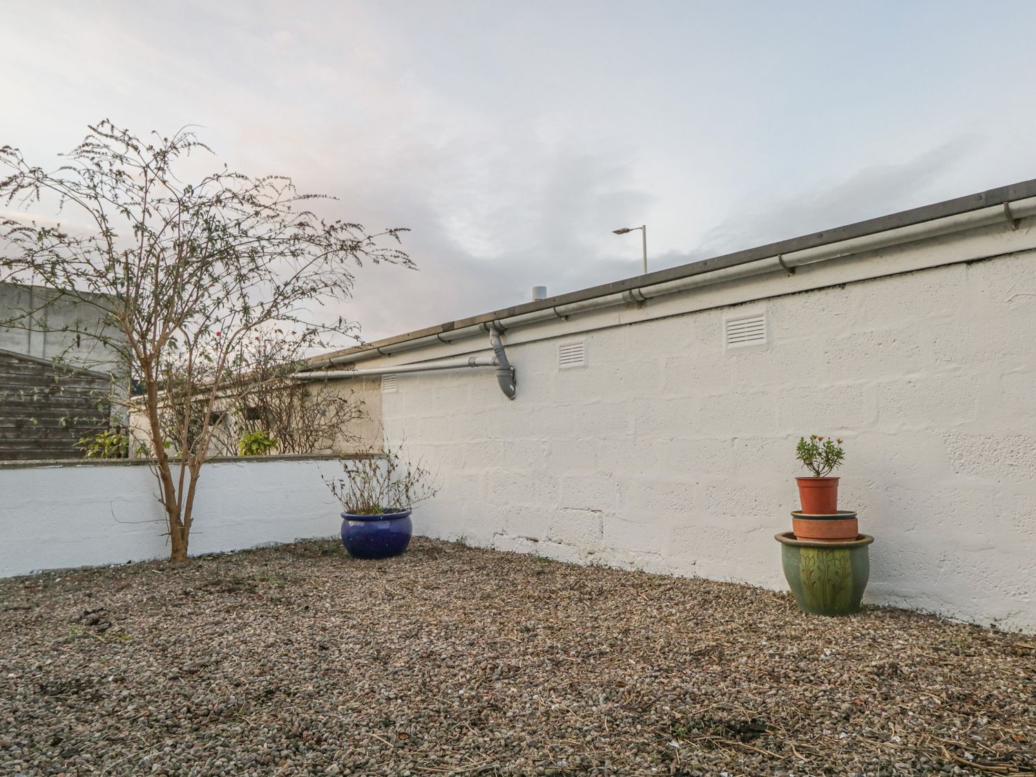 A small garden area with gravel ground and potted plants next to a white wall at The Neuk in Elgin