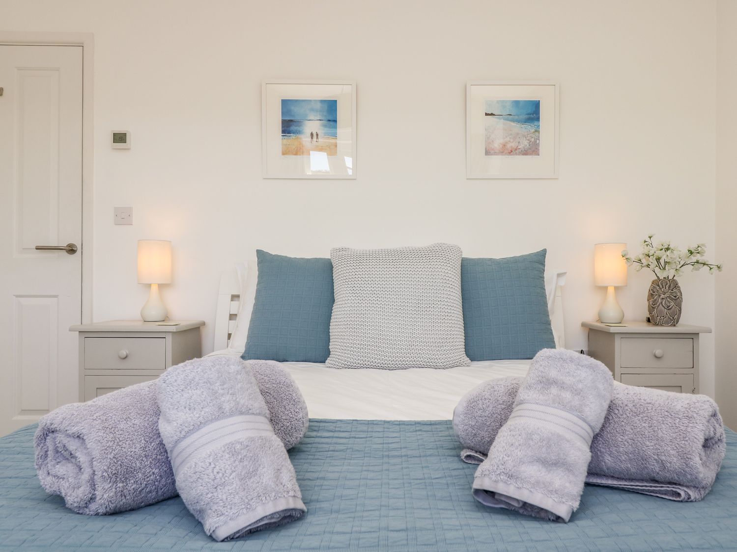 A bedroom with a bed made up with blue and white pillows and rolled towels on the bed at The Upper Deck in Porthcurno