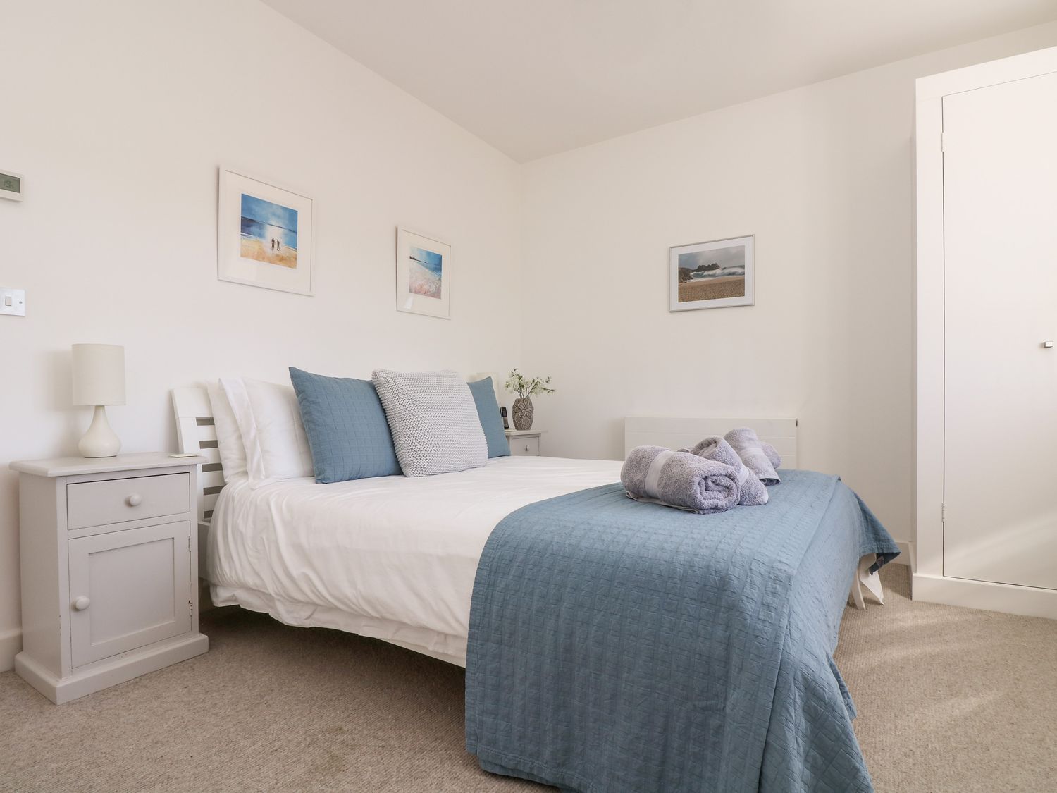 A bedroom with a double bed blue and white bedding two nightstands with lamps and framed pictures on walls at The Upper Deck in Porthcurno