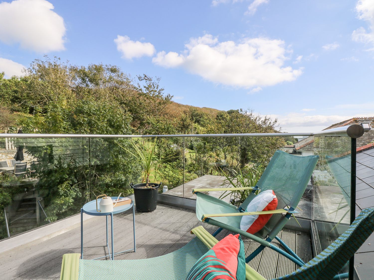 A balcony with two chairs and a small table overlooking trees and hills at The Upper Deck in Porthcurno