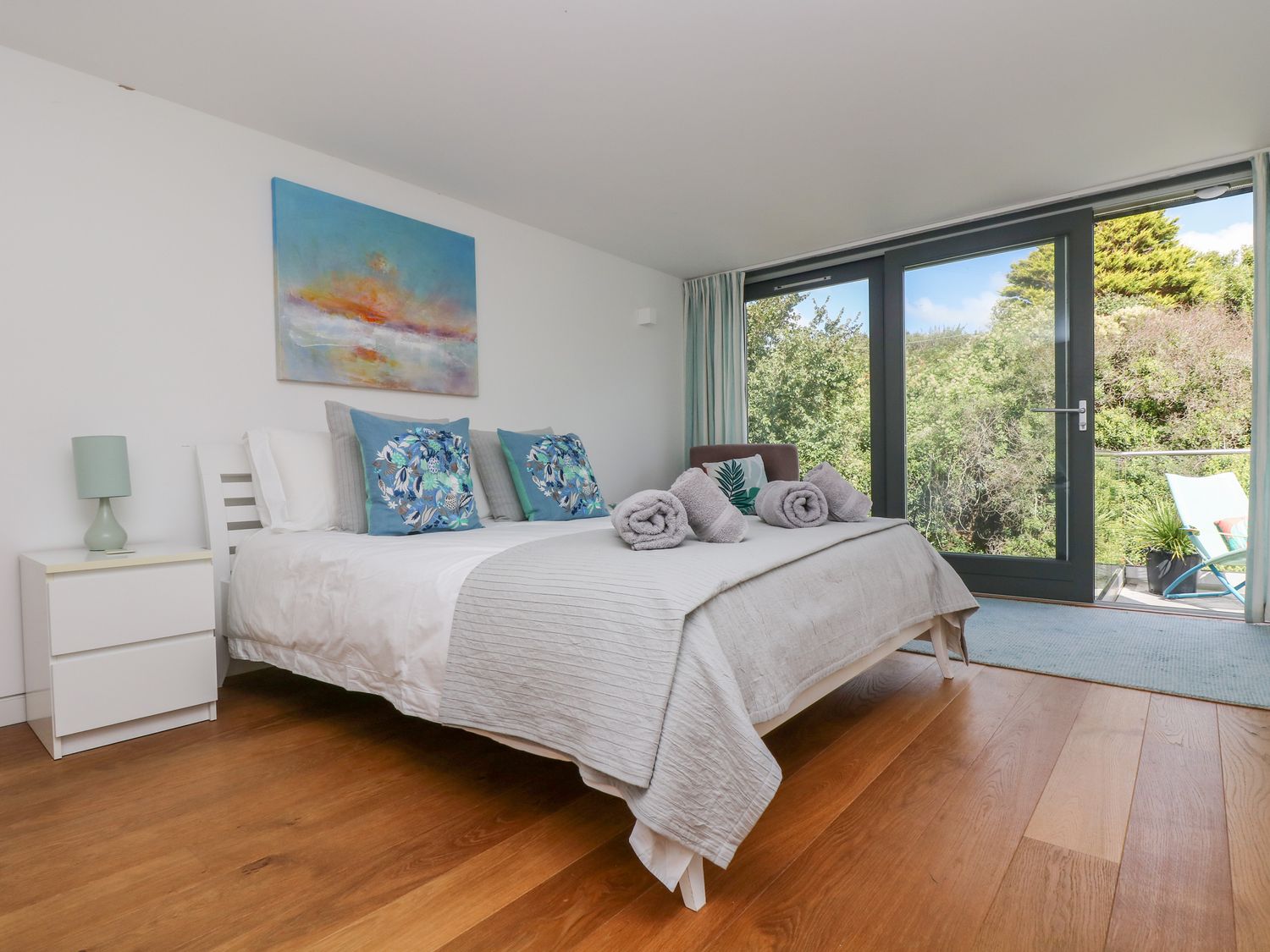 A bedroom with a bed towels and pillows next to glass doors showing outdoor greenery at The Upper Deck in Porthcurno