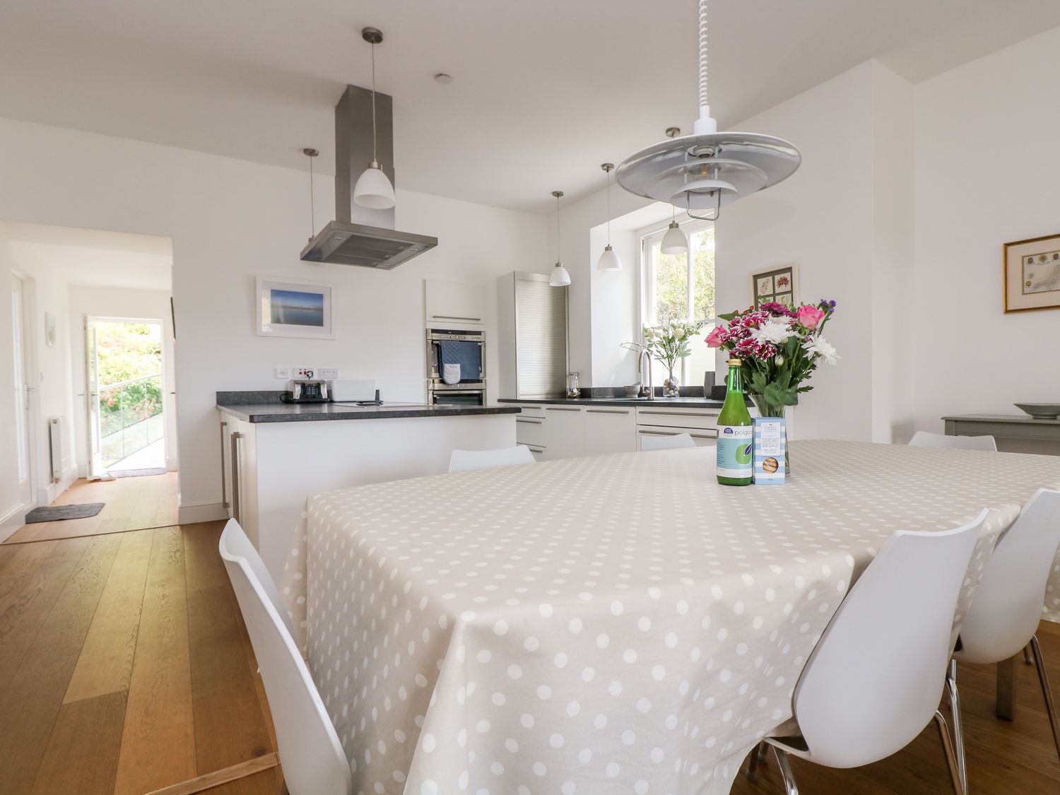 A dining table with a polka dot tablecloth and flowers in a vase in a kitchen at The Upper Deck in Porthcurno