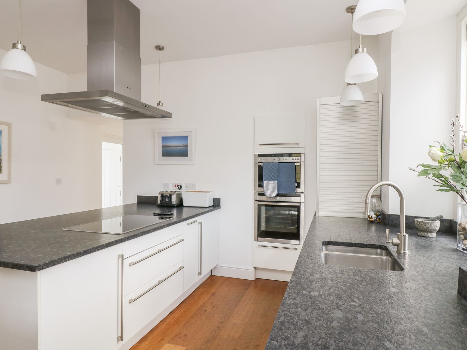 A kitchen with white cabinets dark countertops stainless steel appliances and wooden floor at The Upper Deck in Porthcurno