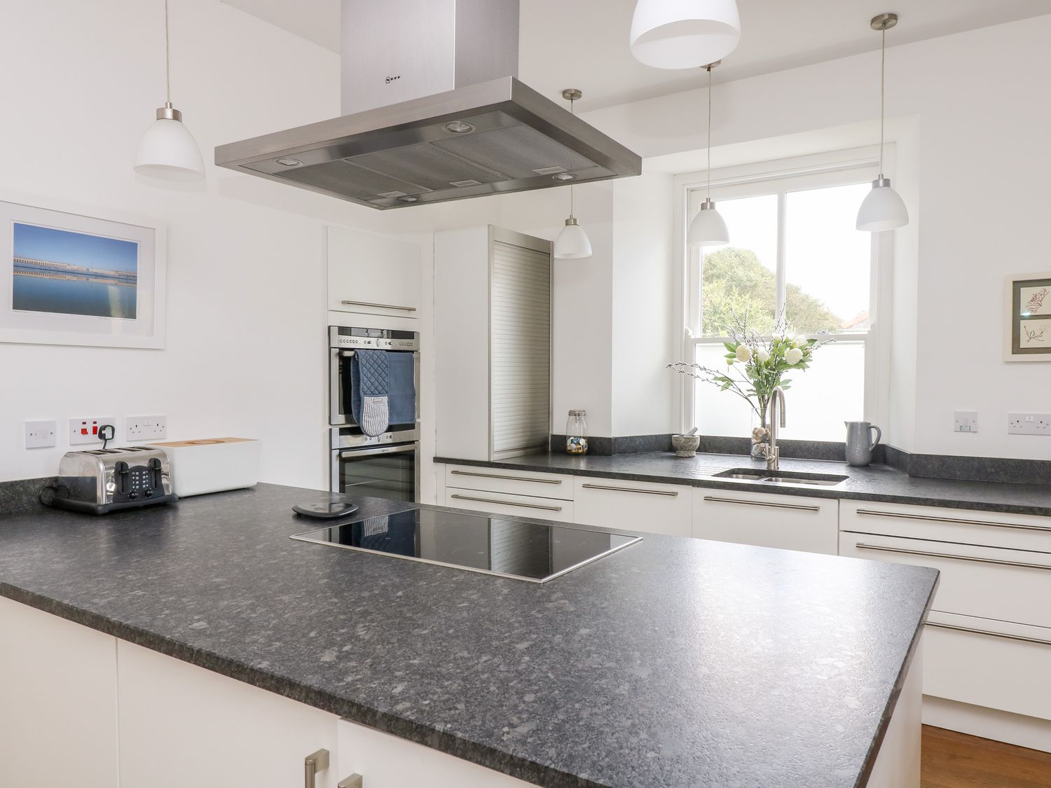 A kitchen with a black countertop island induction cooktop toaster and a vase with flowers on the counter at The Upper Deck in Porthcurno