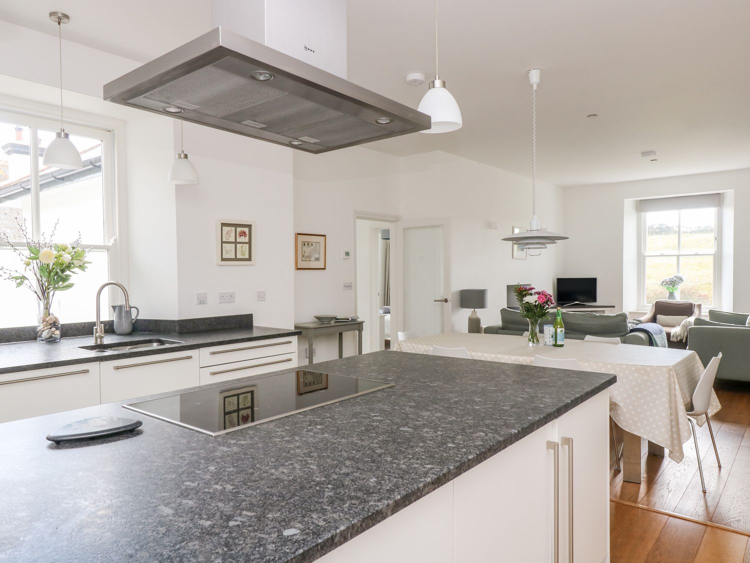 A kitchen with a large island with stovetop and sink beside a dining table with flowers and chairs at The Upper Deck in Porthcurno