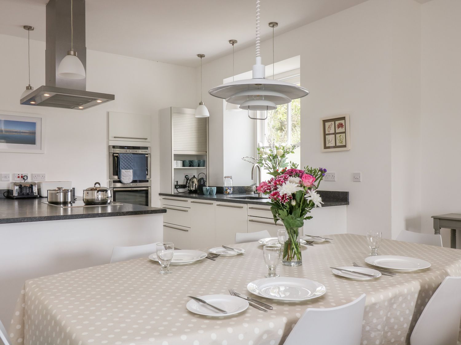 A kitchen with a dining table set with plates and glasses and a flower vase at The Upper Deck in Porthcurno