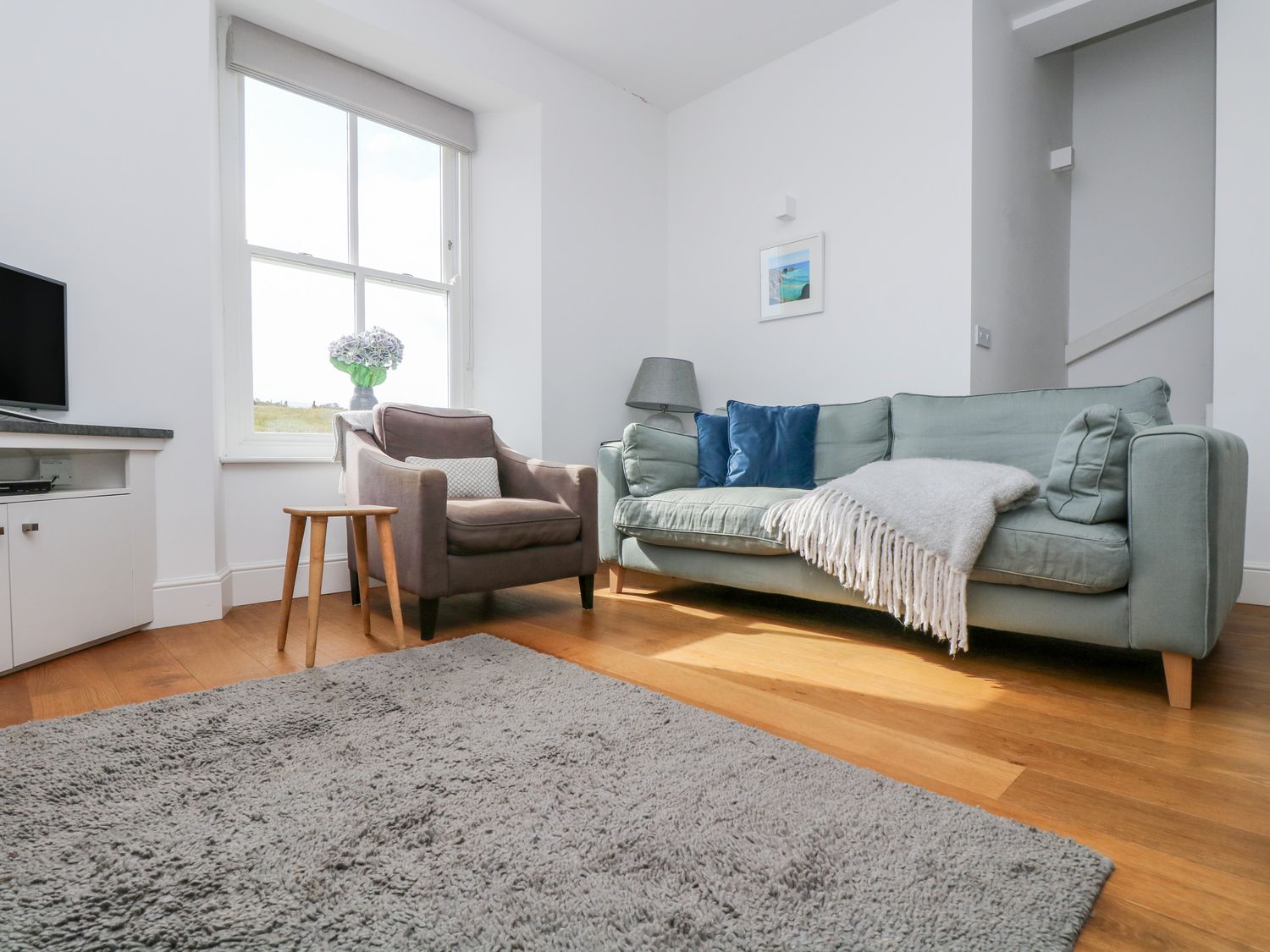 A living room with a sofa and armchair by a window and a gray rug on a wood floor at The Upper Deck in Porthcurno