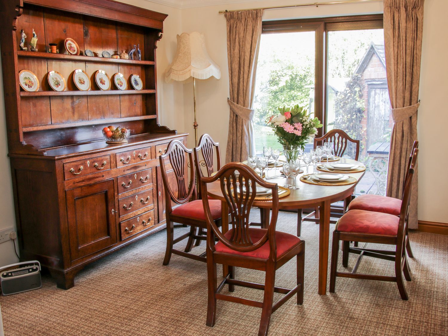 A dining room with wooden table and chairs with red cushions and a wooden cabinet with plates at Court Farm Neen Sollars near Cleobury Mortimer