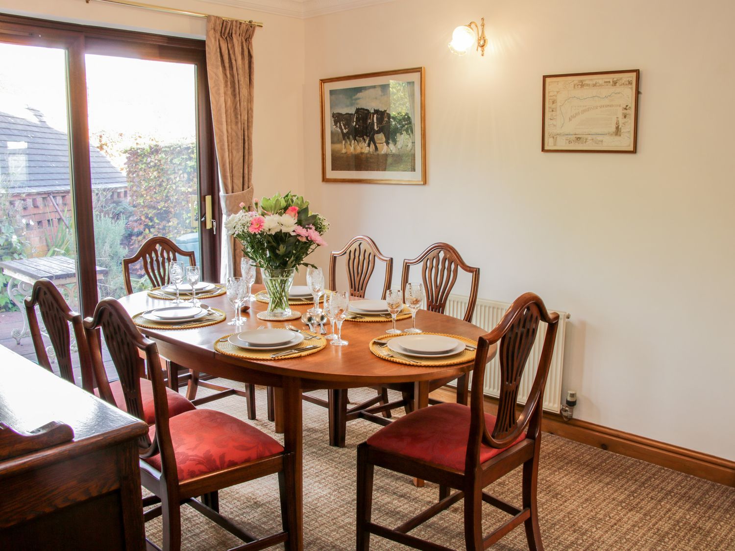 A dining room with a wooden table set for six people flowers in a vase on the table and framed pictures on the wall at Court Farm in Neen Sollars near Cleobury Mortimer