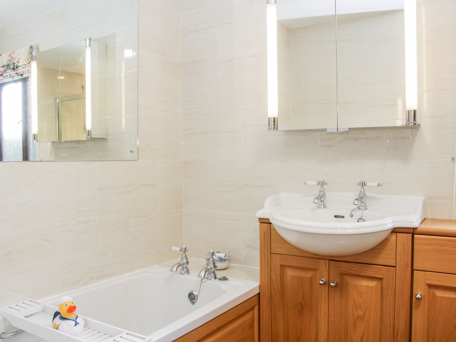A bathroom with a white bathtub and sink with chrome faucets and wooden cabinets at Court Farm Neen Sollars near Cleobury Mortimer