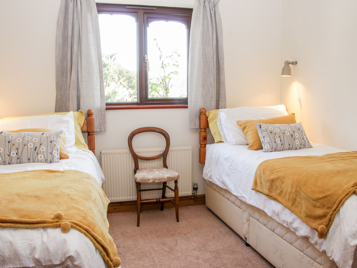 A bedroom with two single beds yellow throws and patterned cushions a wooden chair and a window with curtains at Court Farm in Neen Sollars near Cleobury Mortimer
