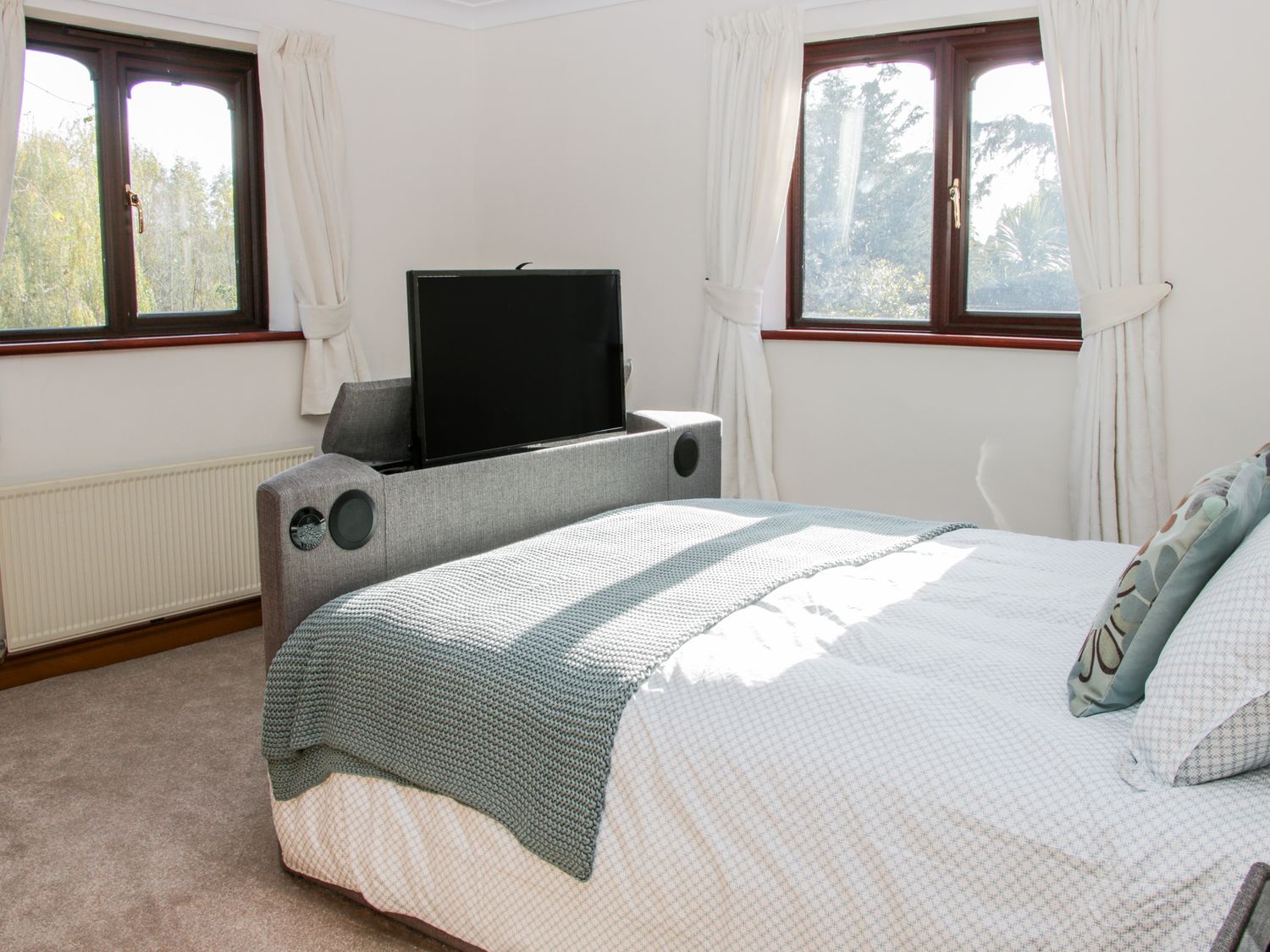 A bedroom with a bed a television on a sofa two windows with curtains at Court Farm in Neen Sollars near Cleobury Mortimer